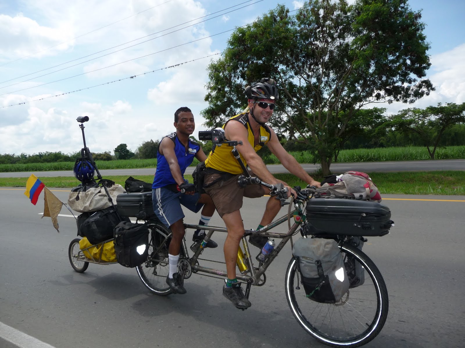 Two riders on a tandem bicycle loaded with expedition gear on a rural road